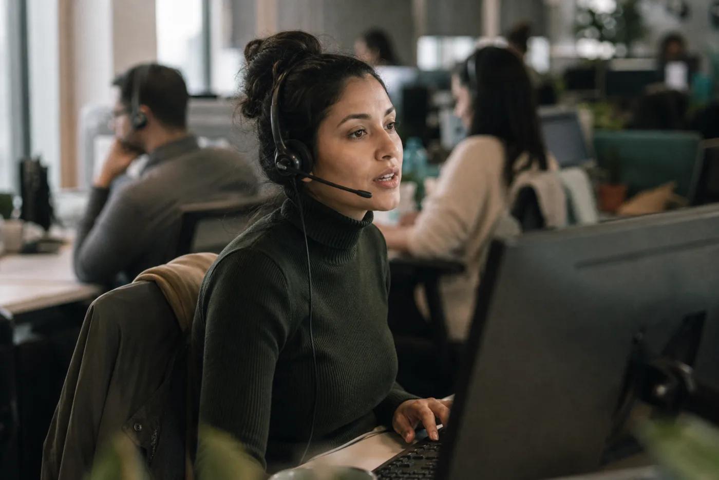 A contact-centre agent on a headset at an open-plan desk, mid-call