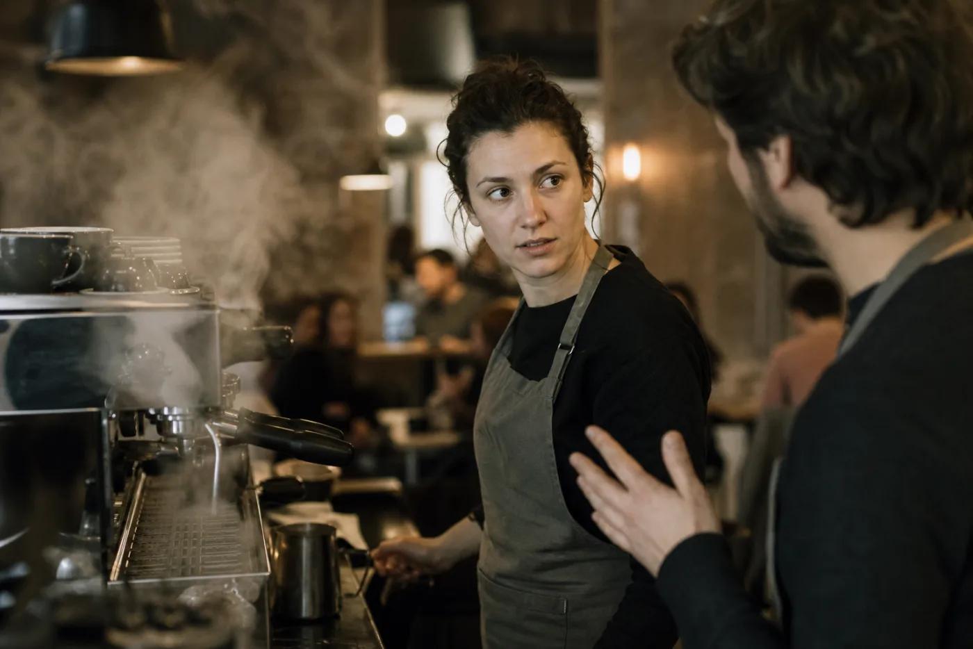 A cafe worker behind the counter, mid-conversation with a colleague during service